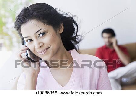 Stock Photography - Portrait of a young woman talking on a mobile phone with a young man sitting in the background. Fotosearch