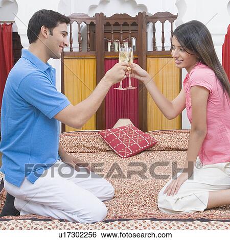 Stock Photograph - Side profile of a young couple toasting with champagne flutes and smiling. Fotosearch