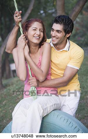 Stock Photo - Young man pushing a young woman on a tire swing. Fotosearch