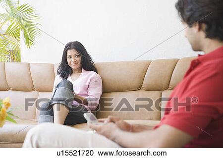 Young woman sitting on a couch and looking at a young man View Large Photo Image Stock Image - Young woman sitting on a couch and looking at a young man. Fotosearch