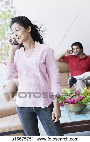 Young woman talking on a mobile phone with a young man sitting in the background View Large Photo Image Stock Image - Young woman talking on a mobile phone with a young man sitting in the background. Fotosearch
