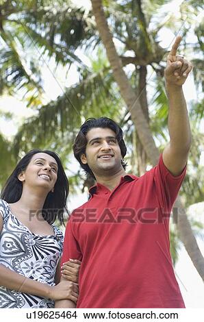 Low angle view of a young man pointing and young woman standing with arm in arm View Large Photo Image Picture - Low angle view of a young man pointing and young woman standing with arm in arm. Fotosearch