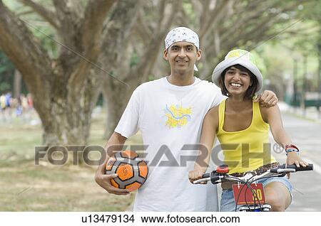Portrait of a young man standing with a young woman riding a bicycle View Large Photo Image Picture - Portrait of a young man standing with a young woman riding a bicycle. Fotosearch