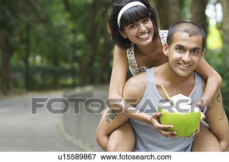 Portrait of a young woman riding piggyback on a young man and holding a coconut View Large Photo Image Stock Photo - Portrait of a young woman riding piggyback on a young man and holding a coconut. Fotosearch