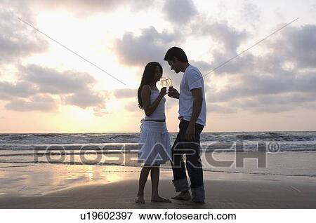 Side profile of a young couple standing on the beach and toasting with champagne flutes View Large Photo Image Stock Photo - Side profile of a young couple standing on the beach and toasting with champagne flutes. Fotosearch