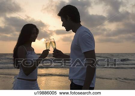 Side profile of a young couple standing on the beach and toasting with champagne flutes View Large Photo Image Stock Photography - Side profile of a young couple standing on the beach and toasting with champagne flutes. Fotosearch