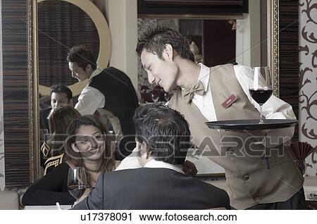 Waiter serving red wine to a young couple in a restaurant View Large Photo Image Stock Image - Waiter serving red wine to a young couple in a restaurant. Fotosearch