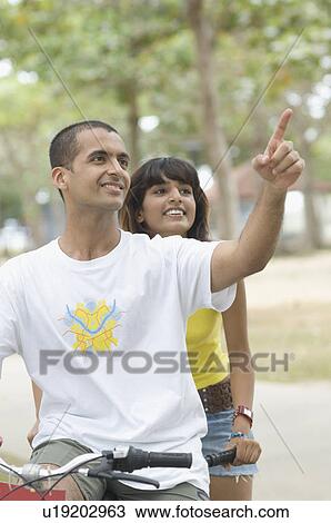 Stock Image - Young couple riding a bicycle and smiling . Fotosearch