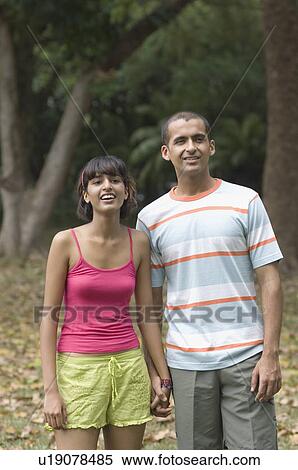 Young couple standing in a park and smiling View Large Photo Image Stock Photography - Young couple standing in a park and smiling . Fotosearch
