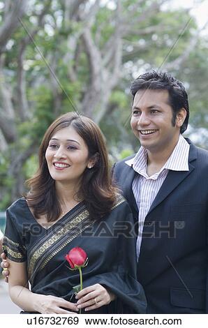 Stock Photo - Young woman holding a rose and smiling with a young man. Fotosearch