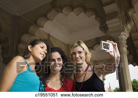 Stock Image - Close-up of a young woman standing with her friends and taking a picture of themselves, Taj Mahal, Agra, Uttar Pradesh, India. Fotosearch