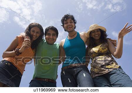 Stock Photo - Low angle view of two young couples standing together and smiling. Fotosearch