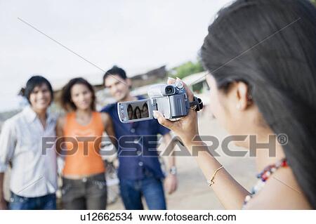 Rear view of a young woman filming her friends with a home video camera View Large Photo Image Picture - Rear view of a young woman filming her friends with a home video camera. Fotosearch