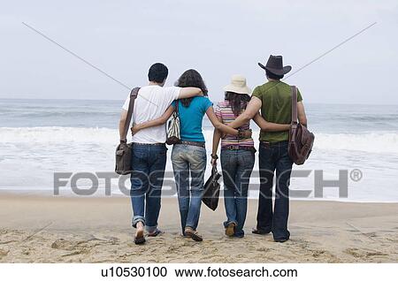 Rear view of two young couples walking on the beach with their arms around each other View Large Photo Image Stock Image - Rear view of two young couples walking on the beach with their arms around each other. Fotosearch
