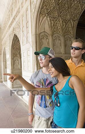 Stock Image - Two young men looking in the direction pointed by a young woman, Taj Mahal, Agra, Uttar Pradesh, India. Fotosearch