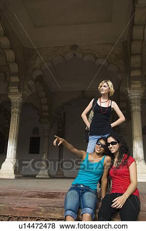 Two young women sitting with their friend standing behind them, Taj Mahal, Agra, Uttar Pradesh, India View Large Photo Image Stock Photo - Two young women sitting with their friend standing behind them, Taj Mahal, Agra, Uttar Pradesh, India. Fotosearch