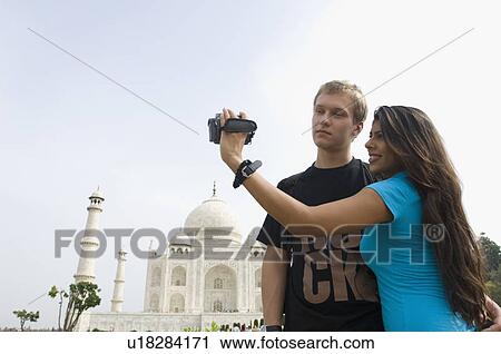 Stock Image - Close-up of a young woman filming and standing with a young man, Taj Mahal, Agra, Uttar Pradesh, India. Fotosearch