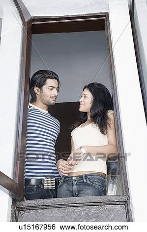 Low angle view of a young couple looking at each other and smiling at a window View Large Photo Image Stock Photograph - Low angle view of a young couple looking at each other and smiling at a window. Fotosearch