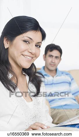 Mid adult woman smiling with her husband sitting on a couch in the background View Large Photo Image Stock Photo - Mid adult woman smiling with her husband sitting on a couch in the background. Fotosearch