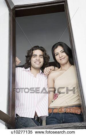 Stock Photography - Portrait of a young couple looking through a window and smiling. Fotosearch