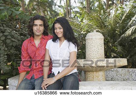 Stock Photograph - Portrait of a young couple smiling on the ledge of a fountain. Fotosearch