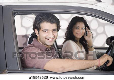 Portrait of a young man driving a car with a young woman talking on a mobile phone View Large Photo Image Stock Photograph - Portrait of a young man driving a car with a young woman talking on a mobile phone. Fotosearch