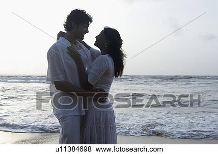 Side profile of a young couple embracing each other on the beach View Large Photo Image Stock Photo - Side profile of a young couple embracing each other on the beach. Fotosearch