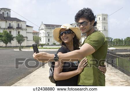 Side profile of a young couple taking a picture of themselves with a mobile phone, Se Cathedral, Goa, India View Large Photo Image Stock Image - Side profile of a young couple taking a picture of themselves with a mobile phone, Se Cathedral, Goa, India. Fotosearch