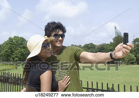 Stock Photo - Side profile of a young couple taking a photograph of themselves, Goa, India. Fotosearch