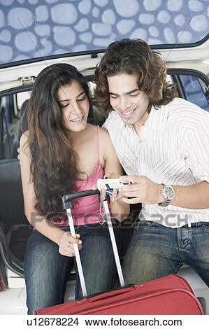 Young couple sitting in a car trunk and looking at a digital camera View Large Photo Image Picture - Young couple sitting in a car trunk and looking at a digital camera. Fotosearch