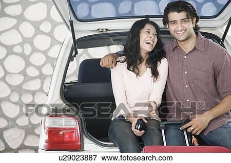 Young couple sitting on the boot of a car and smiling View Large Photo Image Stock Photo - Young couple sitting on the boot of a car and smiling. Fotosearch