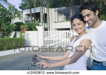 Young couple smiling with a bicycle in front of a house View Large Photo Image Stock Image - Young couple smiling with a bicycle in front of a house. Fotosearch