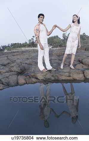 Picture - Young couple standing on rocks and holding their hands. Fotosearch