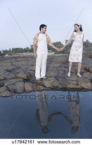 Stock Image - Young couple standing on rocks with holding their hands. Fotosearch
