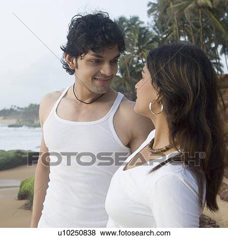 Stock Photo - Young couple standing on the beach and looking at each other, Goa, India. Fotosearch