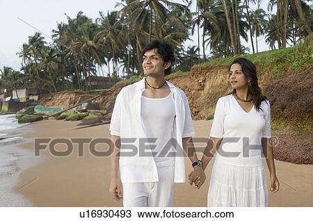 Stock Image - Young couple standing on the beach with holding hands, Goa, India. Fotosearch