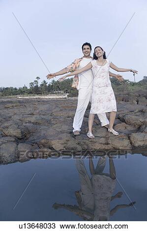 Stock Image - Young couple standing with their arms outstretched and smiling. Fotosearch