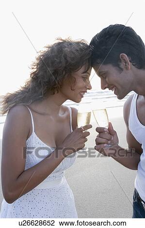 Close-up of a young couple toasting with champagne flutes and smiling View Large Photo Image Stock Image - Close-up of a young couple toasting with champagne flutes and smiling. Fotosearch