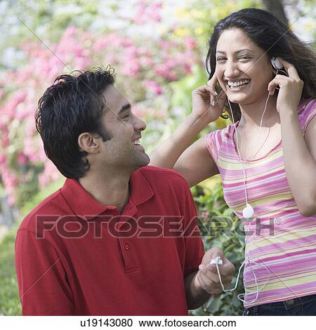 Portrait of a young woman listening to music with an MP3 player and a young man looking at her View Large Photo Image Stock Image - Portrait of a young woman listening to music with an MP3 player and a young man looking at her. Fotosearch