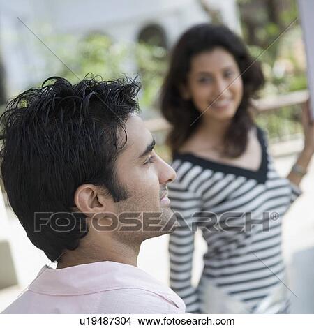 Rear view of a young man smiling with a young woman standing in front of him View Large Photo Image Picture - Rear view of a young man smiling with a young woman standing in front of him. Fotosearch