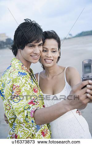 Side profile of a young couple taking a photograph of themselves with a mobile phone View Large Photo Image Stock Image - Side profile of a young couple taking a photograph of themselves with a mobile phone. Fotosearch
