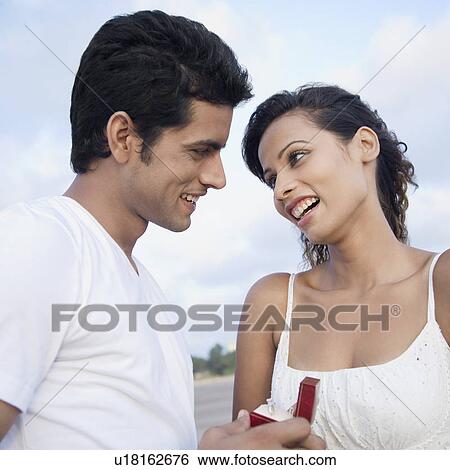 Stock Photograph - Side profile of a young man gifting a ring to a young woman. Fotosearch