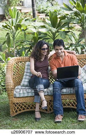 Young man sitting on a couch with a young woman and using a laptop View Large Photo Image Stock Photo - Young man sitting on a couch with a young woman and using a laptop. Fotosearch