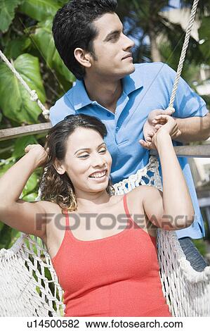 Young woman reclining in a hammock and a young man standing behind her View Large Photo Image Stock Image - Young woman reclining in a hammock and a young man standing behind her. Fotosearch