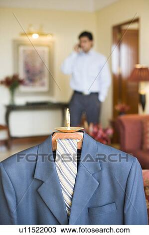 Stock Image - Business suit hanging on a hanger and a businessman talking on a mobile phone. Fotosearch