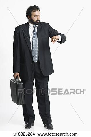 Picture - Businessman holding a briefcase and checking the time. Fotosearch