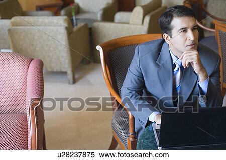 Stock Photography - Businessman sitting in front of a laptop with his hand on his chin. Fotosearch