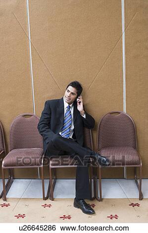 Businessman sitting on a chair and talking on a mobile phone View Large Photo Image Stock Photograph - Businessman sitting on a chair and talking on a mobile phone. Fotosearch