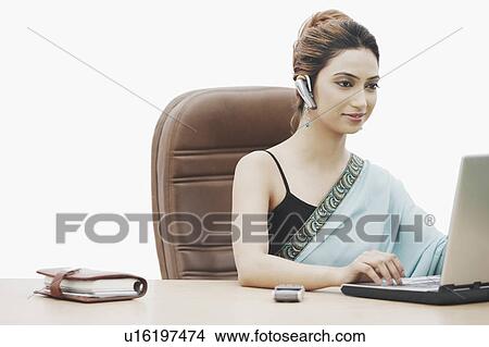Picture - Businesswoman working on a laptop wearing a hands free device. Fotosearch