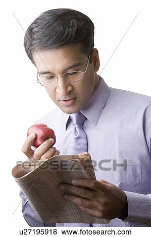Close-up of a businessman eating an apple and reading a newspaper View Large Photo Image Stock Photo - Close-up of a businessman eating an apple and reading a newspaper. Fotosearch